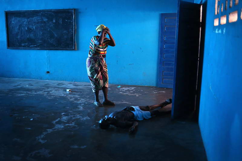 Omu Fahnbulleh stands over her husband Ibrahim after he fell and died in a classroom used for Ebola patients.