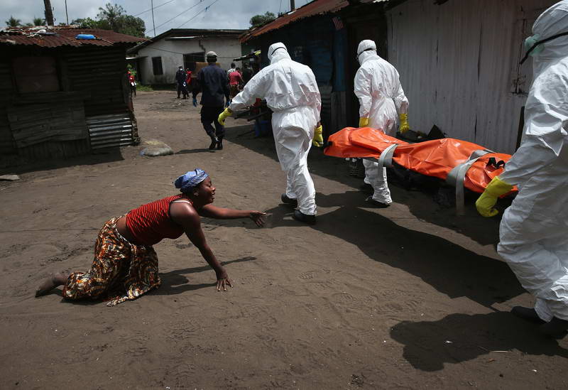 A woman crawls towards the body of her sister as Ebola burial team members take her away.