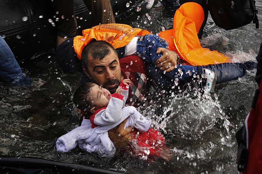 A Syrian refugee holds onto his children as he struggles to walk off a dinghy on the Greek island of Lesbos / Yannis Behrakis, Thomson Reuters - September 24, 2015