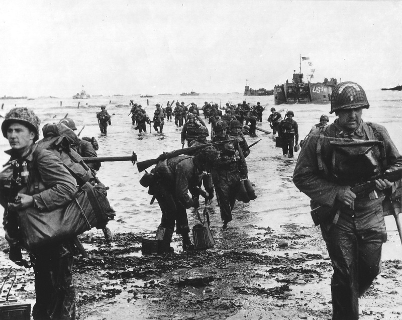“American reinforcements landed at Easy Red on June 6 between 11:30 a.m. and 12:30 p.m. from LCT- 538. Among these troops, sappers from the 37th Engineer Combat Battalion of the 5th Engineer Special Brigade recognizable by the white bow on their helmet. Many men carry in addition to their personal equipment earthmoving tools, ammunition or equipment. The man on the right wears an assault gas mask on his chest in its black neoprene bag”.  6 June, 1944 Easy Red Sector, Omaha Beach, Normandy, France Photographer: unknown or not provided Courtesy Photos Normandie / U.S. National Archives 