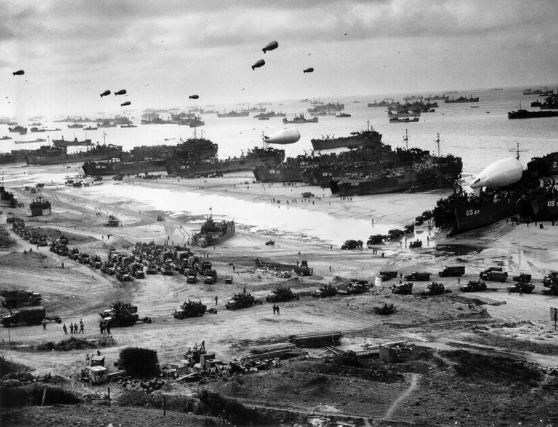 “Supplies Pour Ashore for Invaders of France- This striking panorama ofthe French invasion beach was made by a Coast Guard combat photographer from ahillside cut with the trench (foreground) of the ousted Nazi defenders. The channelwaters are black with shipping, as reinforcements and supplies are funneled ashore forthe conquest of the Cherbourg Peninsula. Balloon barrages float overhead to protect theships from low-flying enemy strafers. One balloon rests on the deck of an LST. Headedinland are long parades of trucks, loaded with troops and supplies”.  June 1944 Normandy, France Photographer: unknown or not provided Courtesy U.S. Navy / U.S. National Archives 