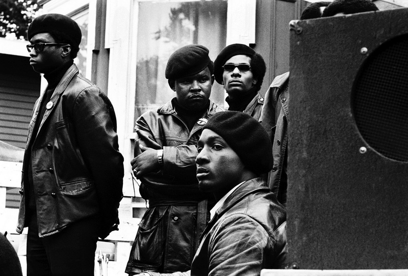 1968. Oakland, California, USA: Pantere Nere ai margini del palco durante una manifestazione per la liberazione di Huey a DeFremery Park. © Stephen Shames