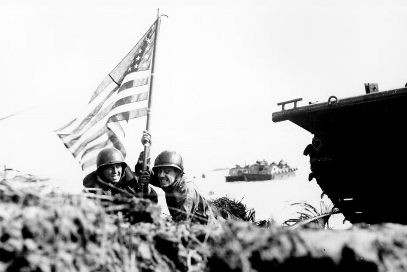 “La Prima bandiera a Guam, agganciata all’albero di una barca. Due ufficiali statunitensi piantano la bandiera americana su Guam otto minuti dopo che le truppe d’assalto dei marine e dell’esercito americano sono sbarcate sull’isola del Pacifico Centrale il 20 luglio 1944” Autore sconosciuto. © Courtesy U.S. National Archives