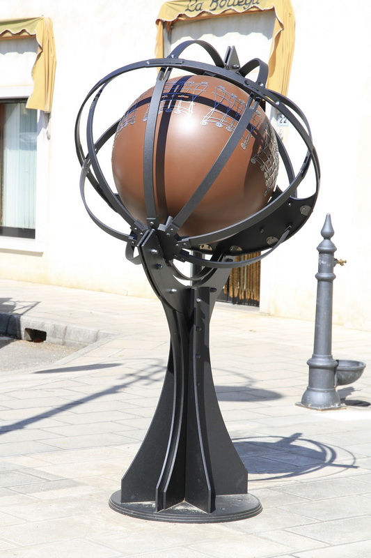 Questa è la celebre Sfera Armillare installata ad Aiello nella piazzetta vicino alla posta. È un orologio solare tridimensionale costituito da una scultura metallica ad anelli che racchiude un globo centrale. Gli anelli esterni e la curvatura del globo permettono di proiettare l'ombra del sole sulla superficie sferica graduata, indicando l'ora solare e il percorso del sole lungo i segni dello zodiaco.